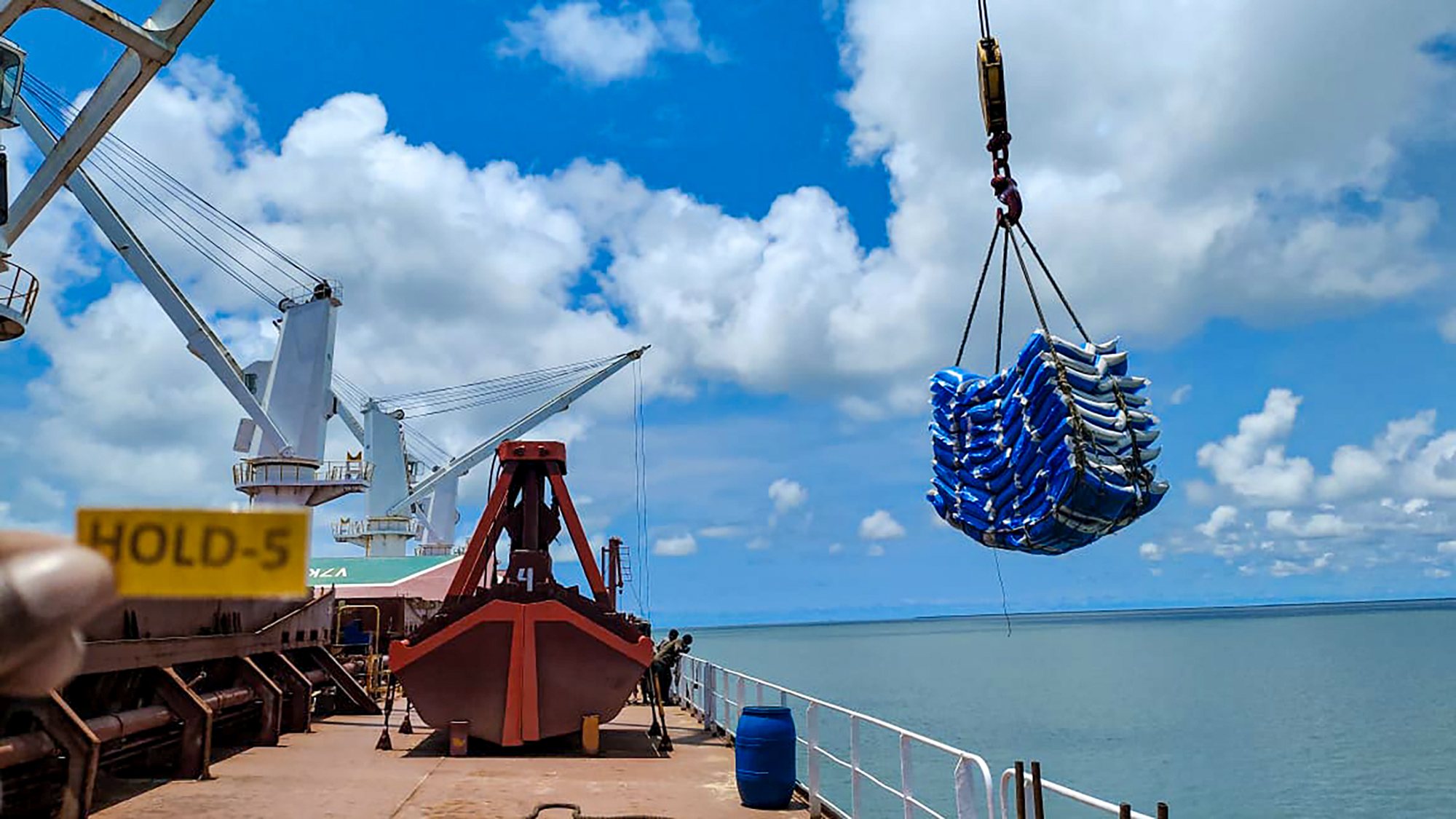 Ship’s crane swinging a sling of bags over an open hatch